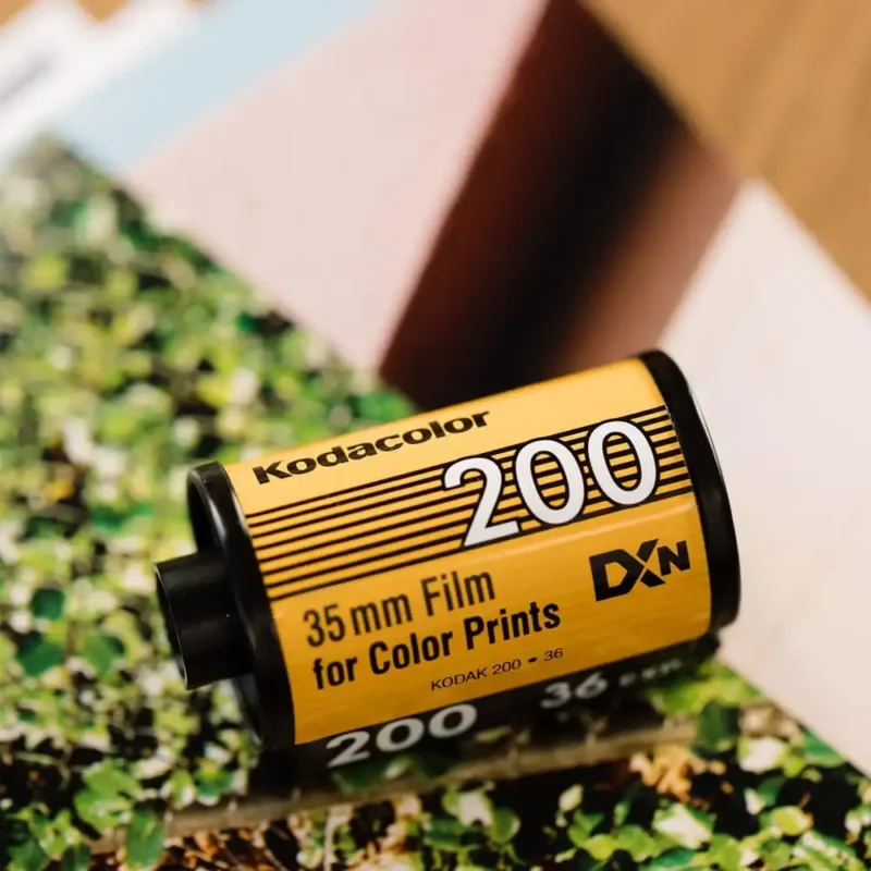 Kodak ColorPlus 200 film canister next to a vintage camera, surrounded by colorful developed photos showcasing the film's warm tones